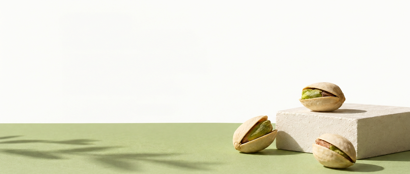 Three pistachios resting on a pale stone block on a soft green surface